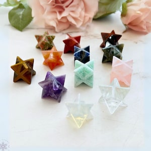 May include: A collection of 12 star-shaped crystal points in various colors, including red, orange, yellow, green, blue, purple, and pink. The crystals are arranged on a white surface.