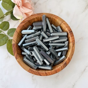 May include: A wooden bowl filled with a large quantity of small, dark gray hematite points. The points are all roughly the same size and shape, and they have a metallic sheen.