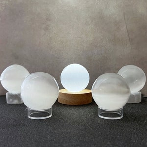 May include: Five white selenite spheres on clear acrylic stands. The center sphere is on a wooden stand.