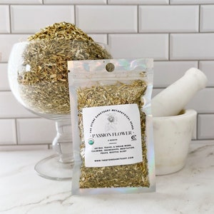 May include: A clear plastic bag with a white label that reads "The Stone Sanctuary Metaphysical Herbs - Passion Flower - 2 ounces" and lists the benefits of passion flower. The bag contains dried passion flower herb.