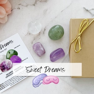 May include: A set of five crystals in a gift box with a gold ribbon. The crystals are selenite, prehnite, lepidolite, amethyst, and clear quartz. The box is labeled "Sweet Dreams" and the crystals are described as promoting peace, relaxation, and restful sleep.