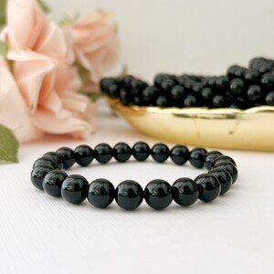 May include: A black onyx beaded bracelet with round beads. The bracelet is on a white surface.