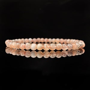 May include: A pink sunstone bracelet with small, round beads. The bracelet is made of natural stones and has a delicate, feminine look.