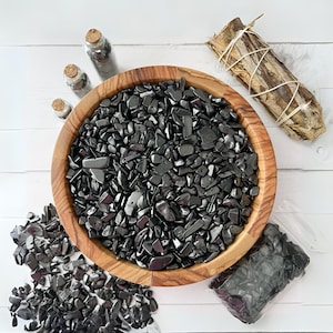May include: A wooden bowl filled with black hematite chips. The bowl is surrounded by smaller piles of the same stones.