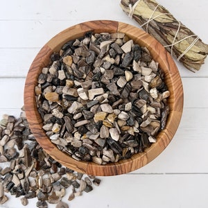 May include: A wooden bowl filled with a variety of small, brown, black, and white petrified wood chips. The bowl is made of light brown wood and has a natural grain pattern.