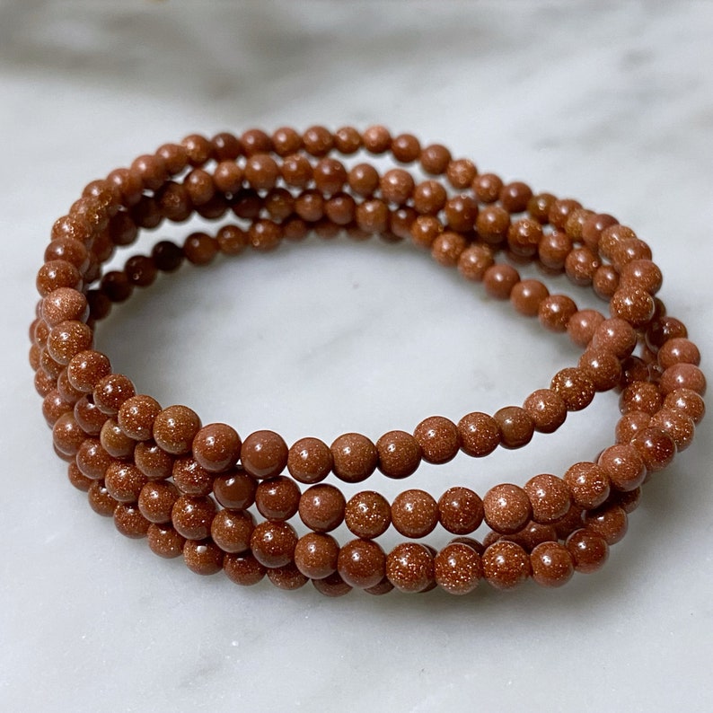 May include: A set of four brown beaded bracelets made of sandstone. The bracelets are stacked on top of each other.