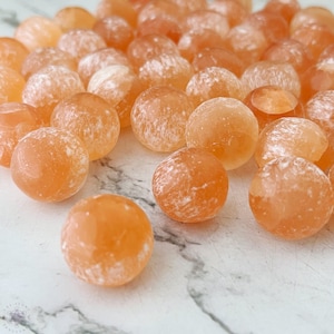 May include: A collection of orange calcite spheres with white markings. The spheres are smooth and polished, and they are arranged in a random pattern.