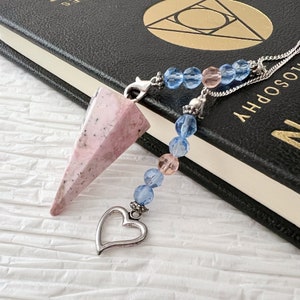 May include: A pink and white crystal pendulum with a silver heart charm and a blue and pink beaded chain.