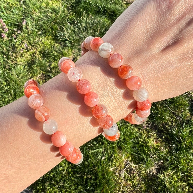 May include: Three stacked bracelets made of orange and white gemstone beads. The bracelets are on a person's wrist.
