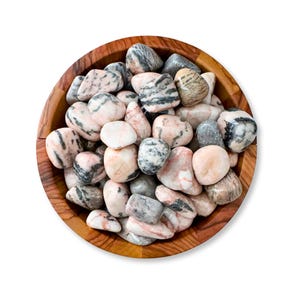 May include: A wooden bowl filled with smooth, polished stones. The stones are a mix of colors, including pink, gray, and white, with unique patterns and textures. The bowl is made of a light brown wood.