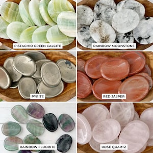 May include: A collection of polished gemstones, including pistachio green calcite, rainbow moonstone, pyrite, red jasper, rainbow fluorite, and rose quartz. Each stone is oval-shaped and displayed in a wooden bowl. Text labels identify each stone type.