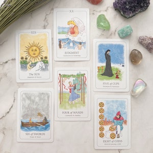 May include: A collection of tarot cards with watercolor illustrations and text. The cards feature images of the sun, a couple dancing, and a figure in a boat. The text includes phrases like "The Sun," "Judgment," and "Six of Swords."