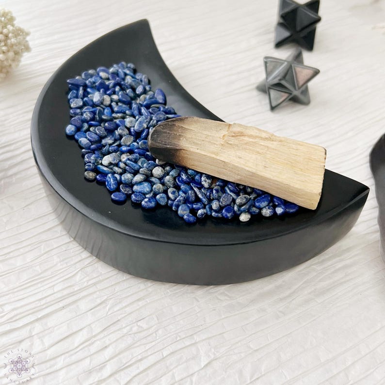 Op de afbeelding: Een zwarte, halve maanvormige schaal gevuld met blauwe lapis lazuli stenen en een palo santo stok.