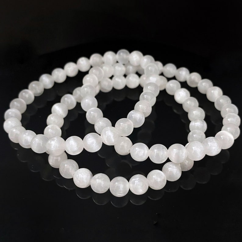 Peut inclure: Trois bracelets en pierres pr&eacute;cieuses blanches avec des perles rondes. Les bracelets sont empil&eacute;s les uns sur les autres.