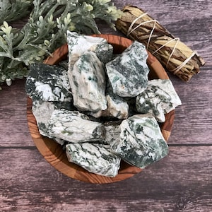 May include: A bowl filled with green and white moss agate tumbled stones. The stones are smooth and polished, with a variety of shapes and sizes.