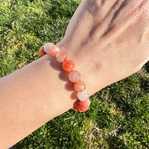 May include: A bracelet made of orange and white gemstone beads. The beads are round and have a smooth, polished finish.
