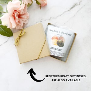 May include: A gold gift box with a gold ribbon is open to reveal a small bag of crystals. The bag is labeled "Confidence & Empowerment Crystals" and lists the crystals as "Carnelian, Sunstone, Citrine, Dragon Stone". The text "Recycled Kraft Gift Boxes Are Also Available" is written below the image.