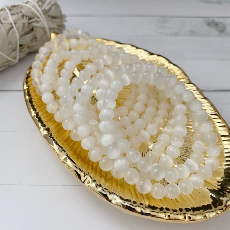 Peut inclure: Un bracelet en pierres blanches avec plusieurs rangs de perles rondes. Le bracelet est pr&eacute;sent&eacute; sur un plat dor&eacute;.