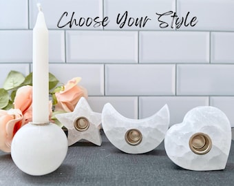 Pode incluir: Castiçais brancos em forma de esfera, estrela, lua crescente e coração. Cada suporte tem uma inserção dourada para uma vela. O texto "Choose Your Style" está escrito em itálico.