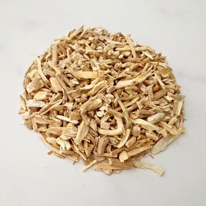 May include: A pile of light brown, dried, chopped roots, possibly for culinary or medicinal use, is displayed on a white surface. The pieces vary in size and shape, with some appearing like small sticks or splinters.