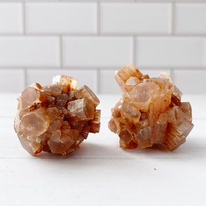 May include: Two brown aragonite crystal clusters, each with a unique shape and texture. The crystals are translucent and have a slightly orange hue.