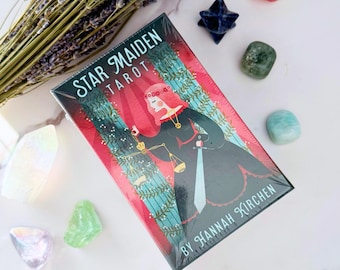 May include: A box of Star Maiden Tarot cards featuring a colorful illustration of a woman in a black dress holding a sword and scales. The box is red with a blue and green background.