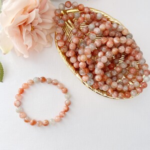 May include: A sunstone bracelet with orange and white beads. The bracelet is made of natural stones and is displayed on a white background.