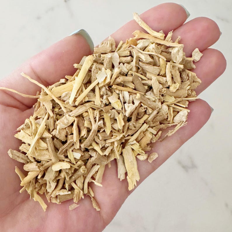 May include: A handful of light brown, chopped wood pieces. The wood pieces are of varying sizes and shapes, with a mix of thin, long splinters and thicker, shorter chunks. The background is a light, neutral color.