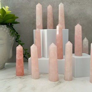 May include: A collection of ten pink rose quartz crystal points arranged on a white platform. The points are various sizes and shapes, with some being more slender than others.