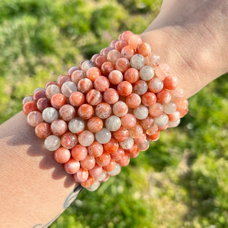 May include: A stack of sunstone bracelets with orange, red, and white beads. The bracelets are made of natural stones and have a polished finish.