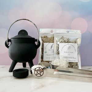 May include: A black cast iron cauldron with a handle, a small charcoal holder, and a pair of tongs with a pentagram design. Two packages of herbs, one labeled "Mugwo" and the other "White Sage", are also included.