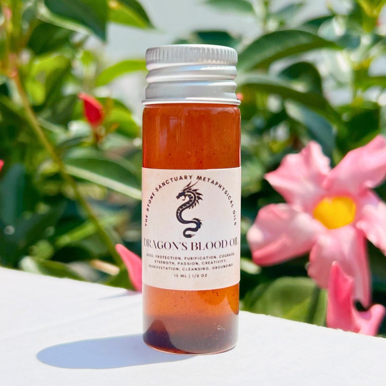May include: A small glass bottle of Dragon's Blood Oil with a silver cap. The label features a black dragon illustration and text. The oil is a reddish-brown colour. The bottle contains 15 ml / 1/2 oz of oil.