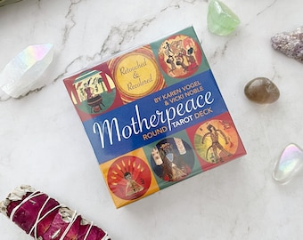 May include: A boxed tarot deck titled "Motherpeace Round Tarot Deck" by Karen Vogel & Vicki Noble. The box features colorful circular illustrations and the words "Retouched & Recolored". The deck is surrounded by crystals and a sage bundle.