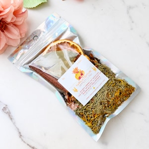 May include: A clear holographic pouch containing a Golden Harvest simmer pot mix with dried orange slices, bay leaves, cinnamon sticks, pink salt, rosemary, and yellow flower petals. A white label features the text Golden Harvest Simmer Pot Mix.