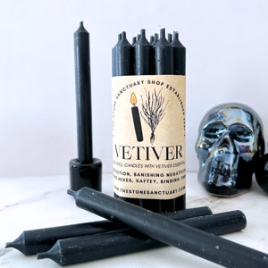 May include: Black spell candles with Vetiver essential oil, with a label that reads "VETIVER" and "THE STONE SANCTUARY SHOP ESTABLISHED 2021". The candles are cylindrical and are displayed with a black skull.
