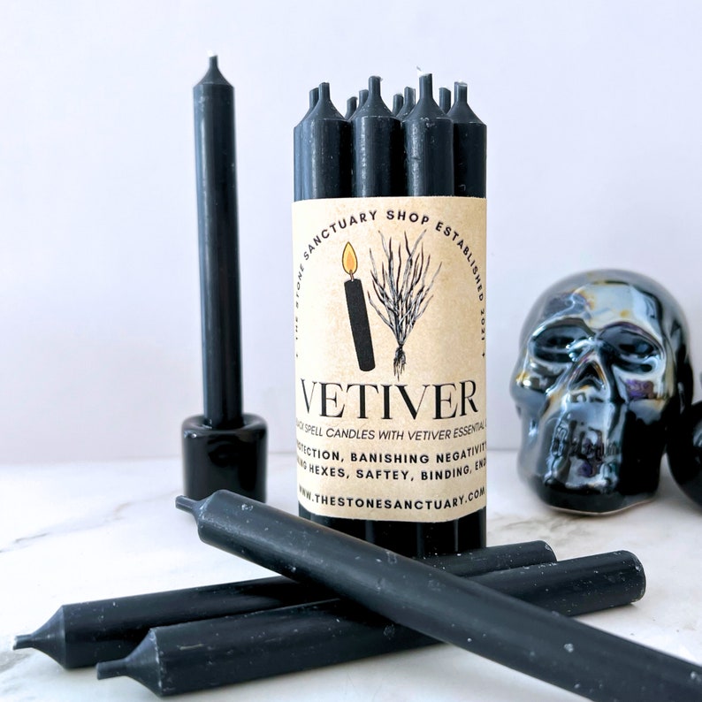 May include: Black spell candles with Vetiver essential oil, with a label that reads "VETIVER" and "THE STONE SANCTUARY SHOP ESTABLISHED 2021". The candles are cylindrical and are displayed with a black skull.