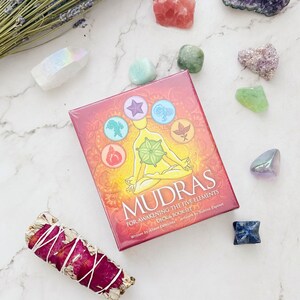 May include: A red box with the title "Mudras: For Awakening the Five Elements Deck & Book Set" written in white. The box features a colorful illustration of a person sitting in a yoga pose with five symbols representing the elements.