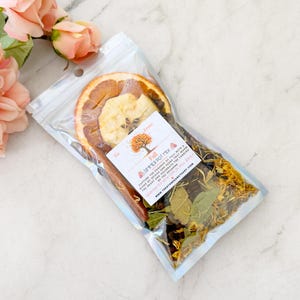 May include: A clear, sealed bag containing a Fall Simmer Pot Mix. The mix includes dried orange and apple slices, cinnamon sticks, and various herbs. A small label reads "Fall Simmer Pot Mix" with text about capturing the essence of fall.