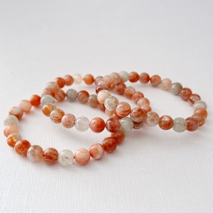 May include: Three stacked bracelets made of orange, white, and brown sunstone beads.