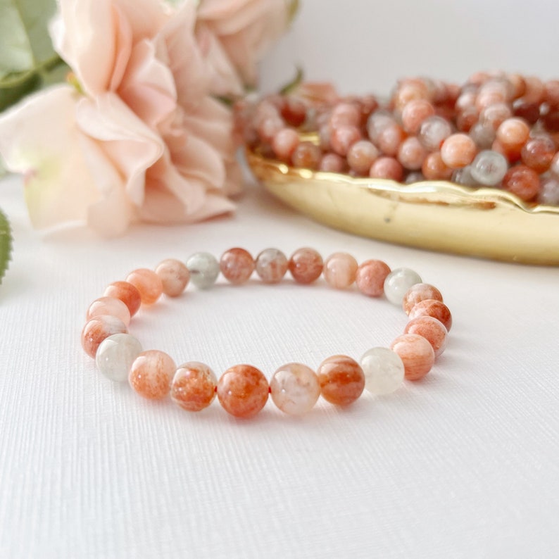 May include: A bracelet made of orange, white, and red sunstone beads. The bracelet is on a white surface.