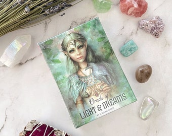May include: A green and blue oracle deck box with a light-skinned fairy with a crown and a raven on her arm. The box has the text "Oracle of Light & Dreams by Scot Howden".