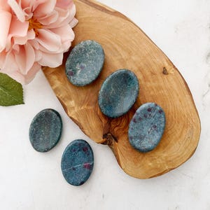 May include: Five oval-shaped green and red gemstone palm stones on a wooden surface.