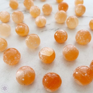 May include: A collection of 20 orange carnelian tumbled stones. The stones are smooth and polished, with a variety of shades of orange and white.