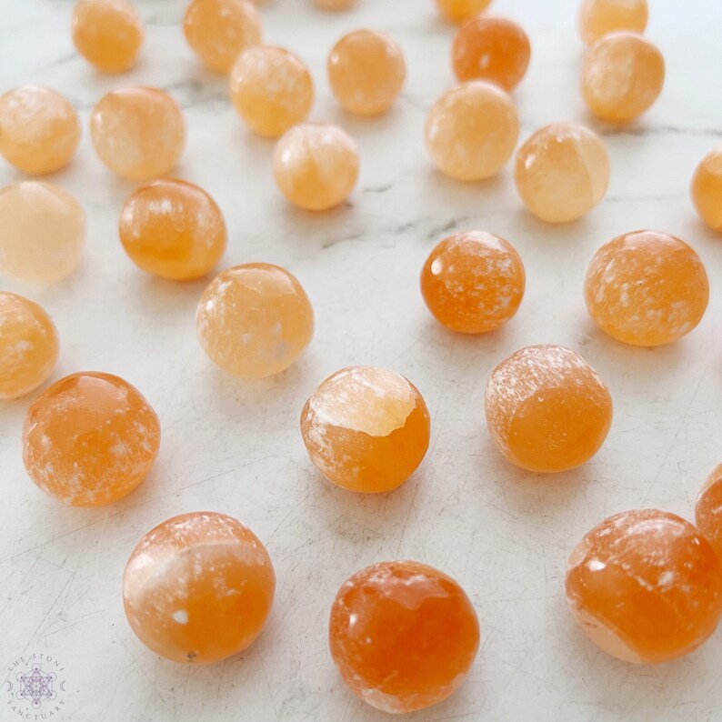 May include: A collection of 20 orange carnelian tumbled stones. The stones are smooth and polished, with a variety of shades of orange and white.