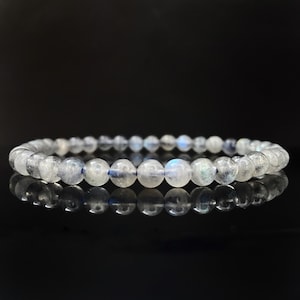 May include: A bracelet made of iridescent white moonstone beads. The beads are round and smooth, and the bracelet is strung on a clear elastic cord.