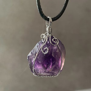 May include: A purple amethyst crystal pendant wrapped in silver wire with a black cord necklace.