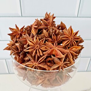 K&ouml;nnte beinhalten: Eine klare Glasschale gef&uuml;llt mit Sternanis. Der Sternanis hat eine tiefrotbraune Farbe und eine sternartige Form. Die Schale steht auf einer wei&szlig;en Oberfl&auml;che mit wei&szlig;en Fliesen im Hintergrund.