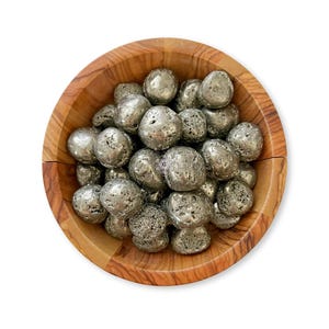 May include: A wooden bowl filled with numerous silver-colored pyrite stones. The pyrite stones have a textured, metallic appearance. The bowl is made of light brown wood with visible grain patterns, set against a white background.