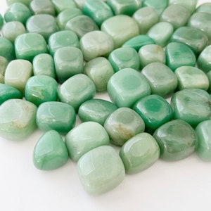 May include: A collection of smooth, light green tumbled stones. The stones are various sizes and shapes, with a polished, glossy finish.