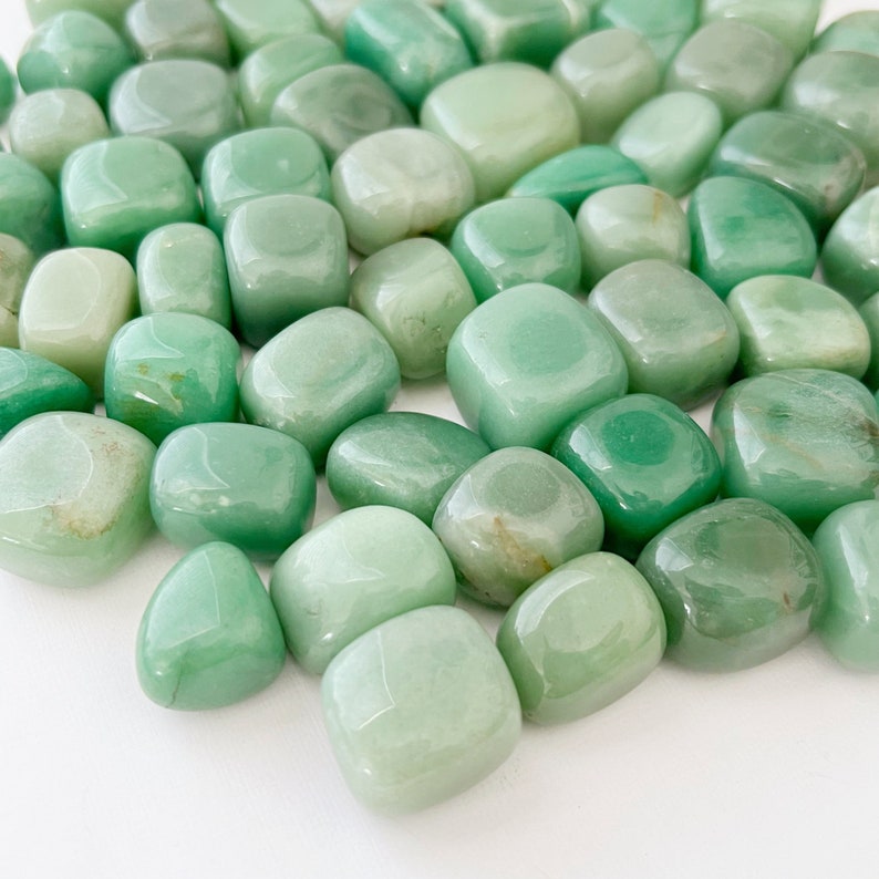 May include: A collection of smooth, light green tumbled stones. The stones are various sizes and shapes, with a polished, glossy finish.
